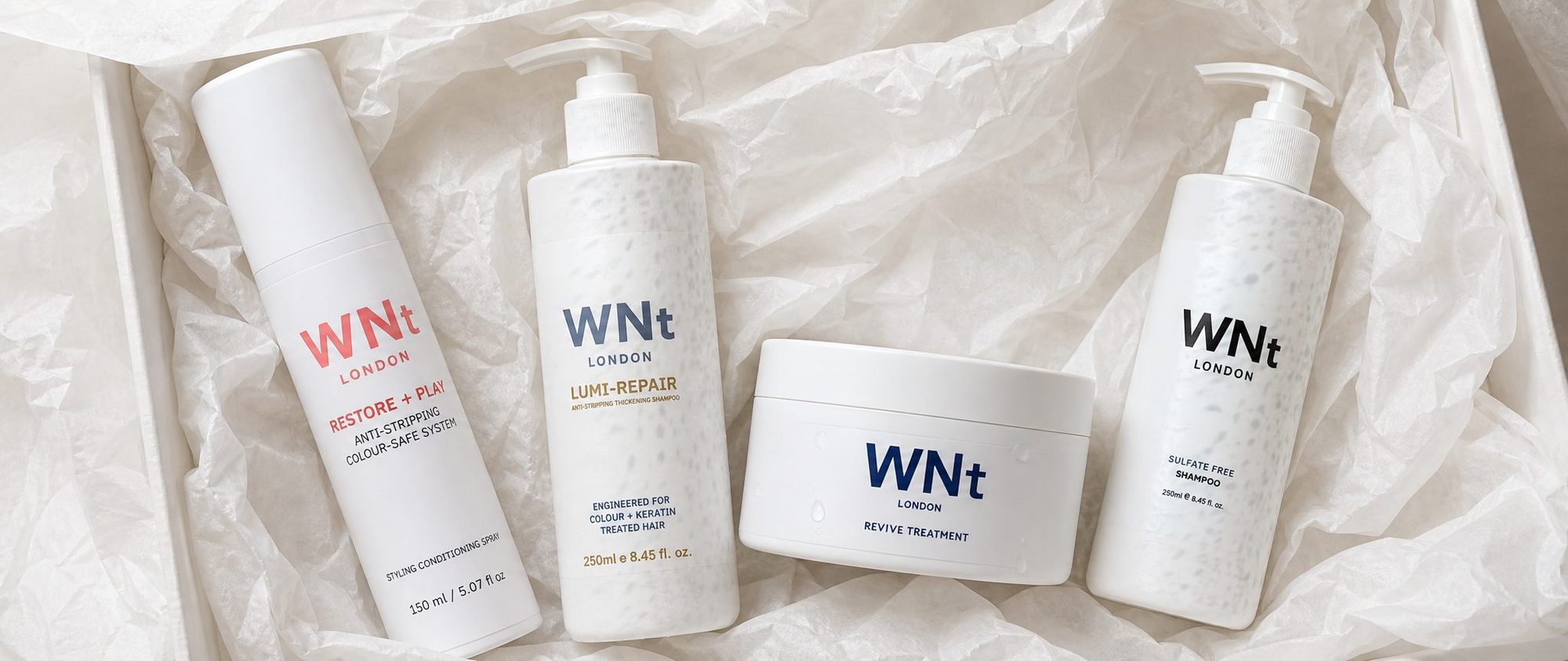 The full WNt range unboxed in white tissue: Restore + Play, Lumi-Repair, Revive Treatment and Sulfate Free Shampoo