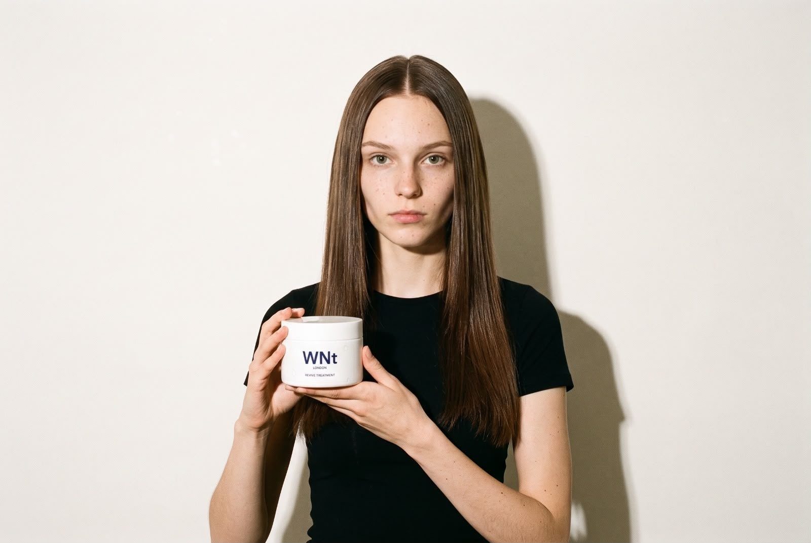 Model with long, straight brown hair holding WNt Revive Treatment with both hands